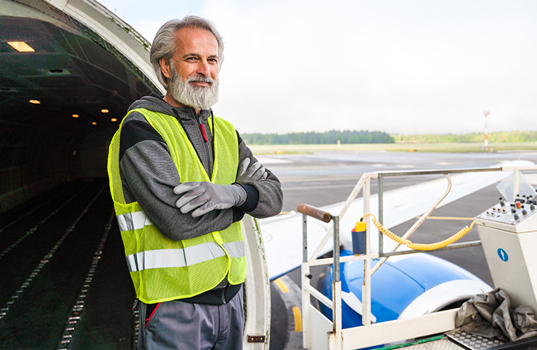 Ein Frachtabfertiger steht vor einem Frachtflugzeug und zeigt, dass der Beruf auch f&uuml;r Quereinsteiger geeignet ist.