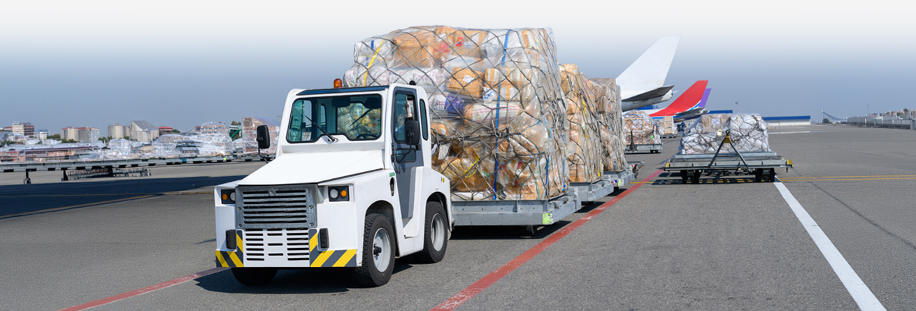 Ein Schlepper transportiert mehrere Luftfrachtcontainer &uuml;ber das Vorfeld und bringt sie zum wartenden Flugzeug.