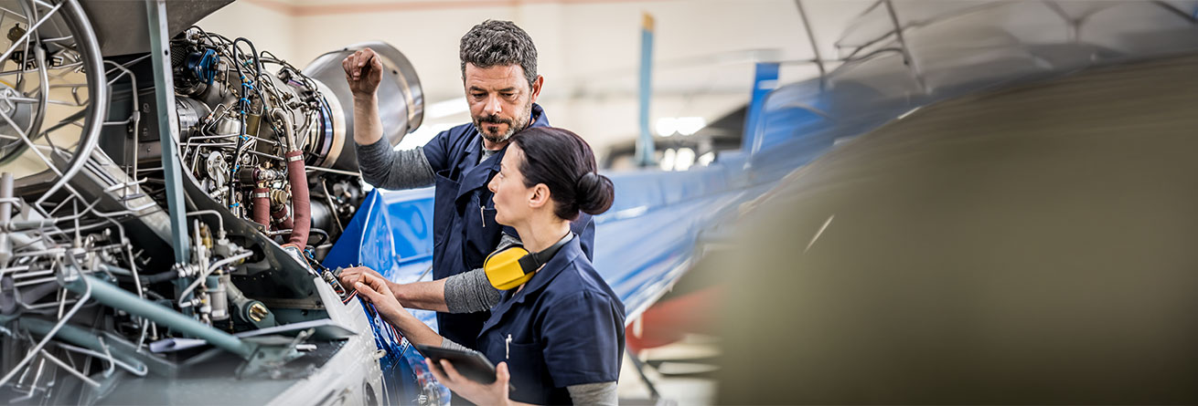 Zwei Flugger&auml;tmechaniker pr&uuml;fen gemeinsam ein Flugzeugtriebwerk, besprechen technische Details und dokumentieren Wartungsma&szlig;nahmen.