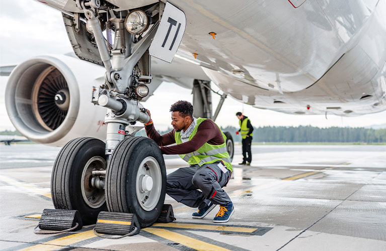 Ein Flugger&auml;tmechaniker kontrolliert das Fahrwerk eines Flugzeugs und f&uuml;hrt Inspektions- sowie Wartungsarbeiten vor dem Flugbetrieb durch.