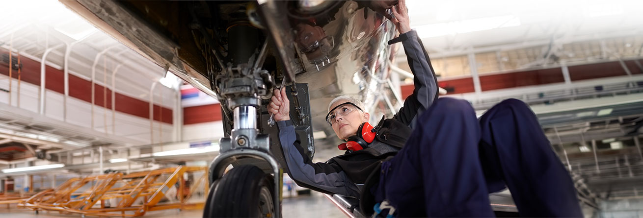Ein Flugger&auml;tmechaniker f&uuml;hrt Wartungs- und Instandhaltungsarbeiten an der Unterseite eines Flugzeugs durch und &uuml;berpr&uuml;ft sicherheitsrelevante Bauteile.