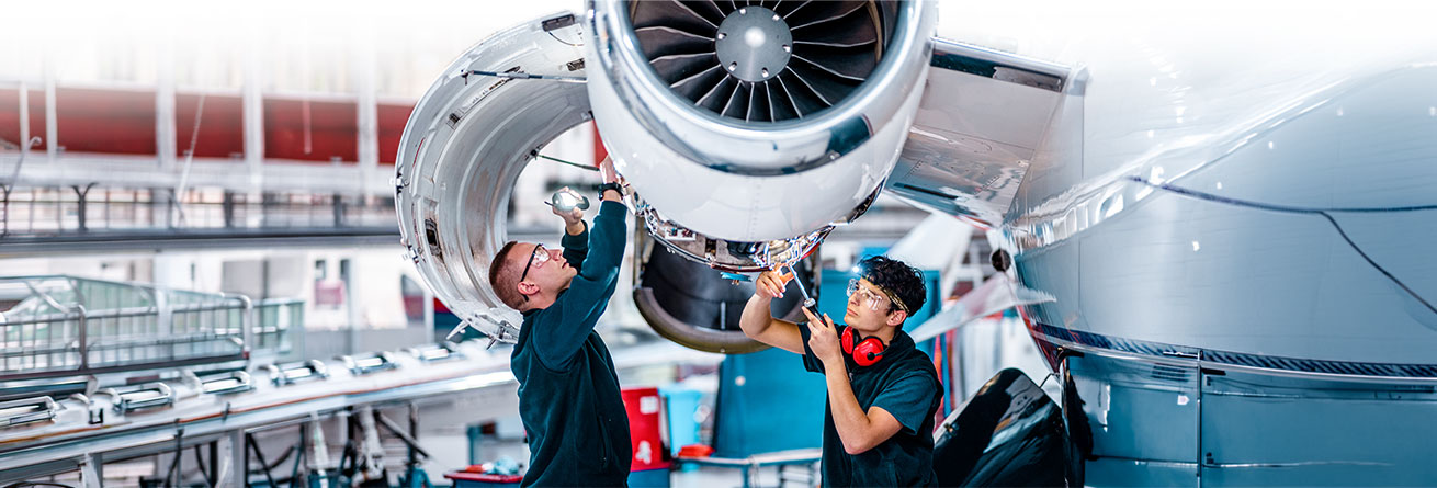 Zwei Flugger&auml;tmechaniker arbeiten gemeinsam an einem Flugzeugtriebwerk, tauschen ihr Fachwissen aus und sorgen f&uuml;r die sichere Einsatzbereitschaft des Luftfahrzeugs.