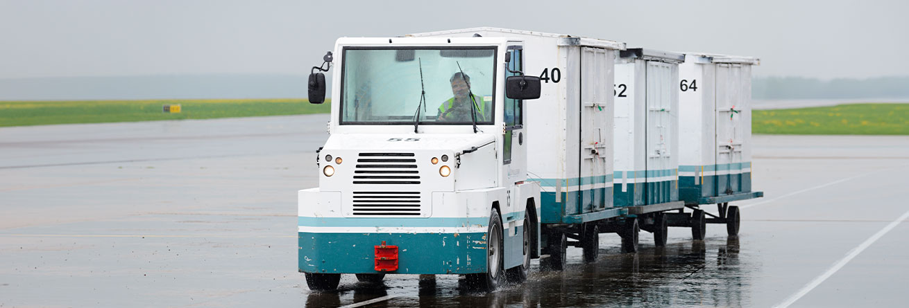 Ein Gep&auml;ckschlepper transportiert Gep&auml;ckcontainer &uuml;ber das Vorfeld und sorgt f&uuml;r eine p&uuml;nktliche und zuverl&auml;ssige Gep&auml;ckabfertigung am Flughafen.