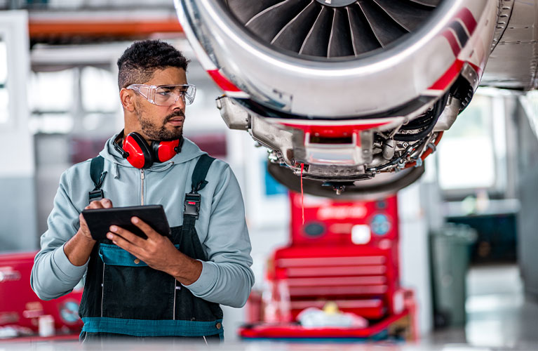 Ein Flugger&auml;tmechaniker &uuml;berpr&uuml;ft ein Flugzeugtriebwerk, dokumentiert Wartungsarbeiten digital und sorgt f&uuml;r die sichere Einsatzbereitschaft des Luftfahrzeugs.