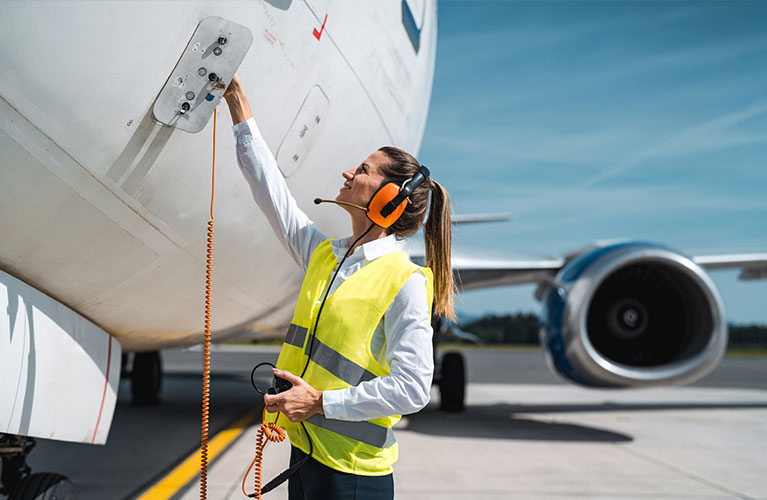 Kommunikation am Flugzeug Flughafenmitarbeiterin in Warnweste und Gehörschutz bedient ein Anschlusskabel an einem Flugzeug.