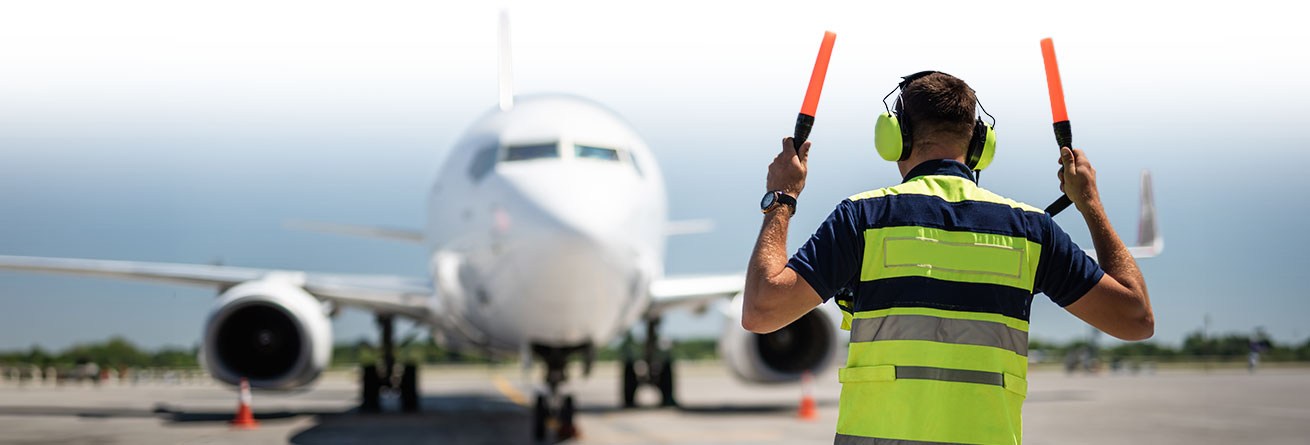 Einweiser auf dem Rollfeld Flughafenmitarbeiter in Warnweste und Gehörschutz weist ein ankommendes Flugzeug mit Leuchtstäben ein.