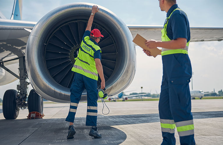 Ausbildung am Triebwerk Supervisor überprüft ein Flugzeugtriebwerk, während ein Auszubildender mit Klemmbrett daneben steht.
