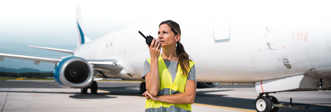 Koordination am Flugzeug Flughafenmitarbeiterin in Warnweste spricht über Funkgerät vor einem abgestellten Passagierflugzeug.