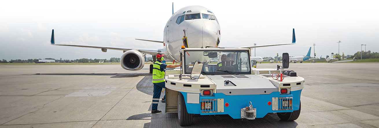 Flughafenfahrzeug schiebt ein Passagierflugzeug zurück, Mitarbeiter koordiniert den Ablauf.