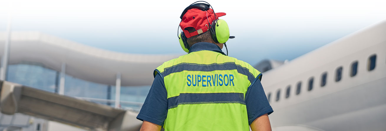 Flughafen-Supervisor in Warnweste mit Aufschrift 'Supervisor' überwacht die Flugzeugabfertigung.