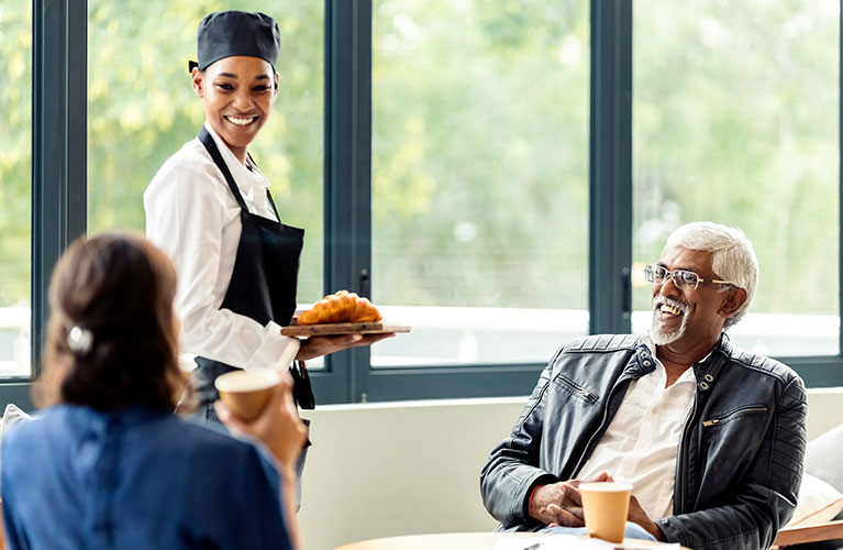 Lächelnde Servicekraft serviert Gebäck an Gäste in einem Café oder Restaurant.